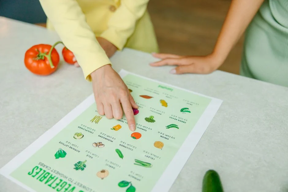 Close-up of hands pointing to a vegetable nutrition chart with fresh tomatoes on the table.